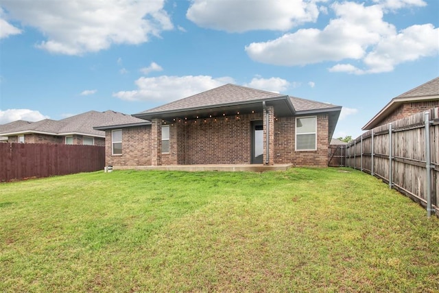 rear view of property with brick siding, a fenced backyard, and roof with shingles