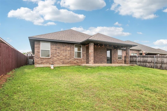 rear view of property with roof with shingles, brick siding, a fenced backyard, a yard, and a patio