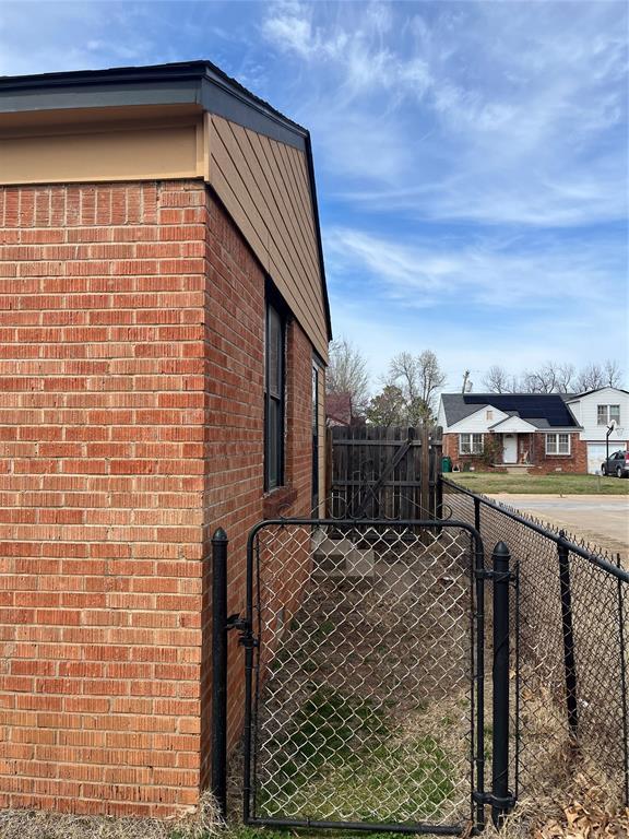 view of side of home featuring brick siding, a gate, and fence