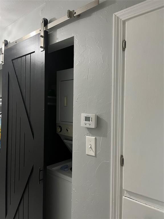 washroom with a textured wall, a barn door, and stacked washer and clothes dryer