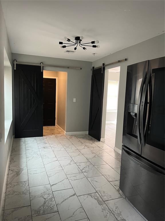 unfurnished living room with baseboards, a barn door, and marble finish floor
