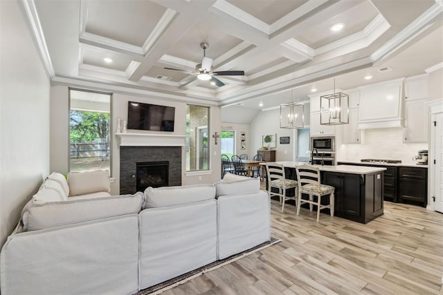 living area with crown molding, beam ceiling, a fireplace, light wood finished floors, and ceiling fan with notable chandelier