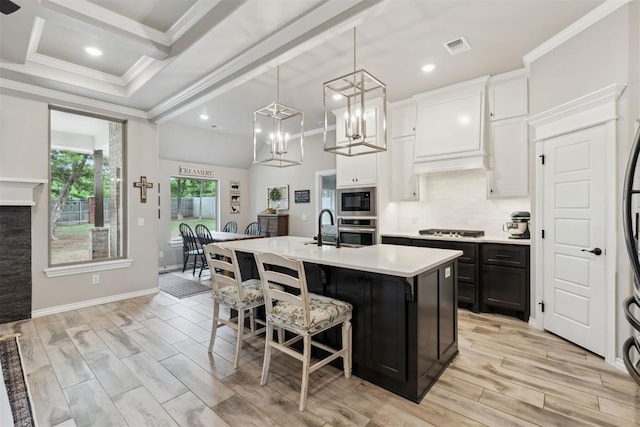 kitchen with crown molding, a sink, light countertops, stainless steel appliances, and a center island with sink