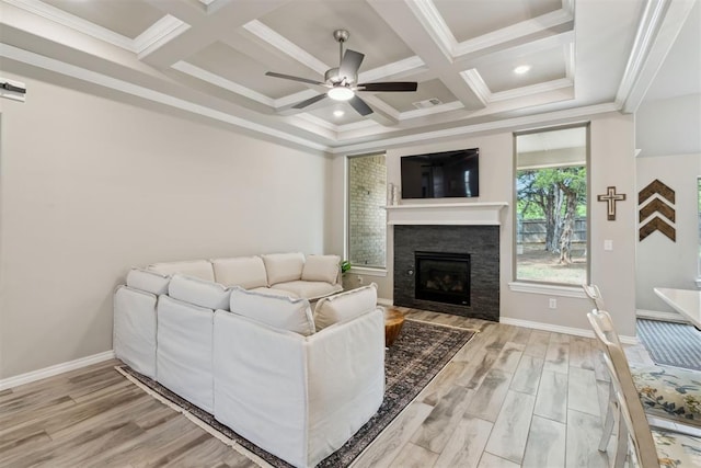 living room with a ceiling fan, beamed ceiling, light wood finished floors, a glass covered fireplace, and coffered ceiling
