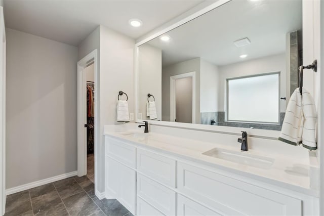 bathroom featuring baseboards, double vanity, a walk in closet, and a sink