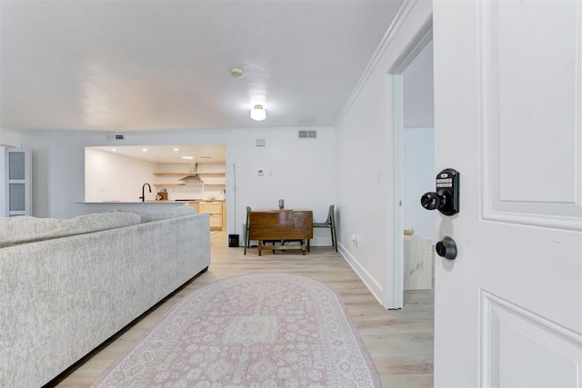 entryway with light wood-style floors, baseboards, ornamental molding, and visible vents