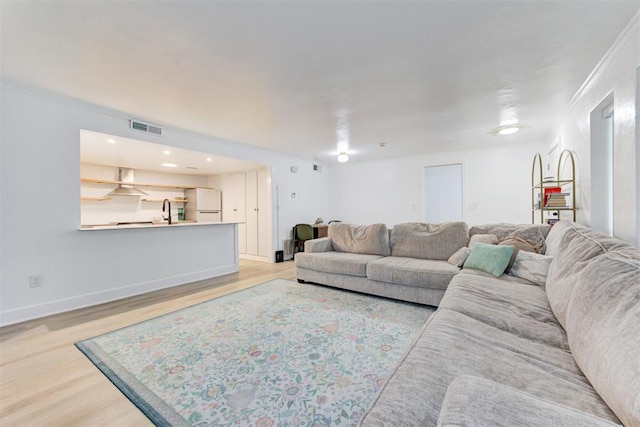 living area featuring baseboards, visible vents, ornamental molding, and light wood finished floors