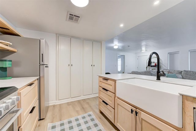 kitchen with visible vents, a sink, open floor plan, light wood-style floors, and light brown cabinets