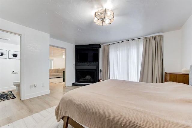 bedroom featuring baseboards, ensuite bathroom, a fireplace, and light wood finished floors