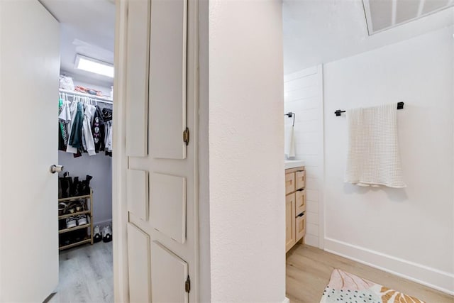 bathroom featuring a walk in closet, visible vents, wood finished floors, vanity, and baseboards