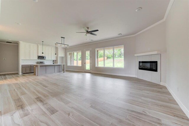 unfurnished living room with crown molding, a tiled fireplace, light wood-style flooring, a ceiling fan, and baseboards
