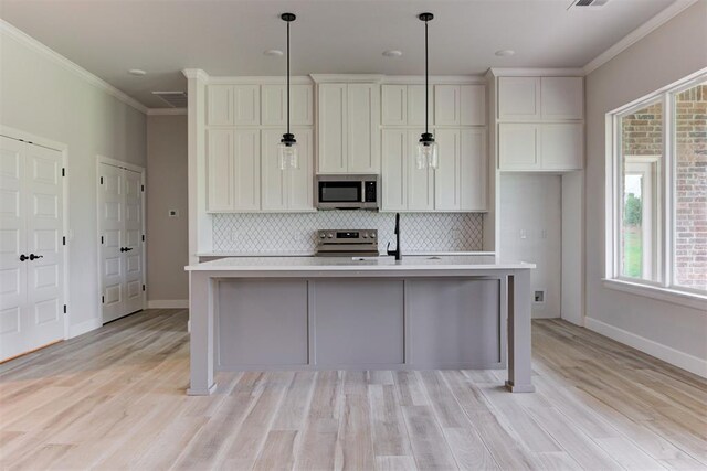 kitchen with crown molding, appliances with stainless steel finishes, light countertops, a kitchen island with sink, and tasteful backsplash