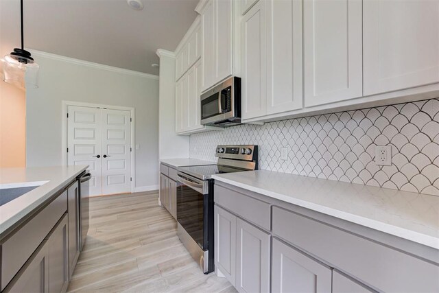 kitchen with decorative backsplash, crown molding, light countertops, light wood-style floors, and stainless steel appliances