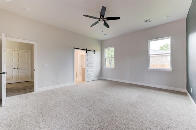 unfurnished bedroom featuring a ceiling fan, visible vents, a barn door, baseboards, and carpet