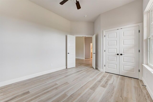 unfurnished bedroom with light wood-type flooring, a ceiling fan, baseboards, and a closet
