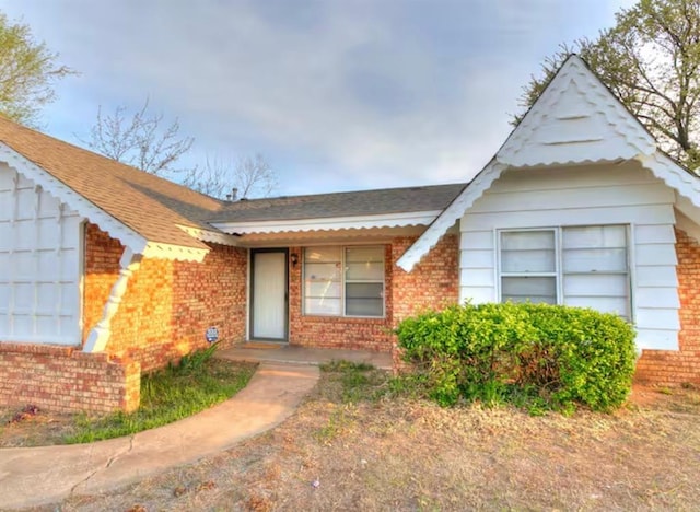 view of front of property with a shingled roof and brick siding