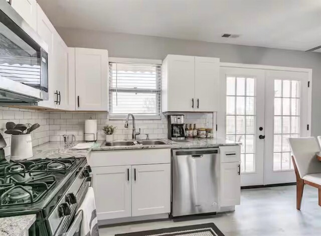 kitchen featuring white cabinets, a sink, french doors, stainless steel appliances, and decorative backsplash