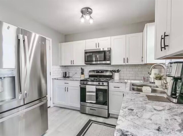 kitchen with tasteful backsplash, light stone countertops, a sink, white cabinets, and stainless steel appliances