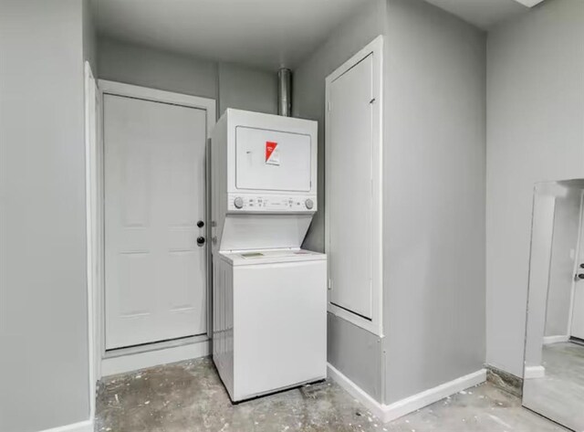 clothes washing area with baseboards, laundry area, and stacked washer / dryer