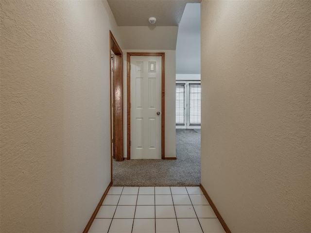 hallway with light colored carpet, a textured wall, and baseboards