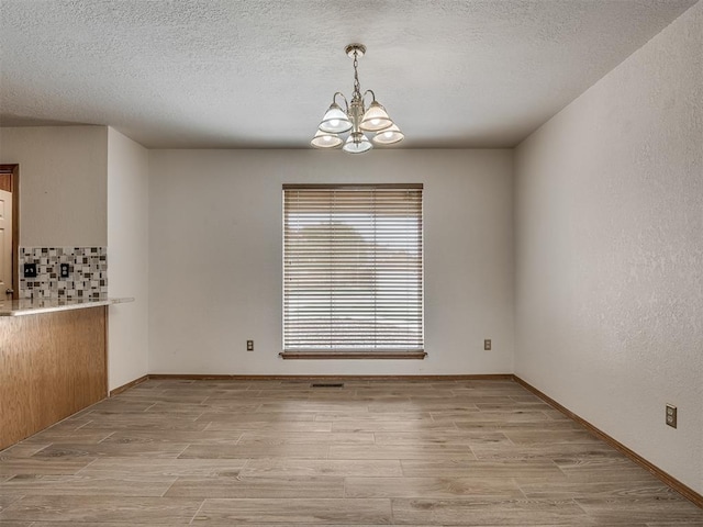 unfurnished dining area featuring light wood-type flooring, a textured ceiling, baseboards, and a notable chandelier