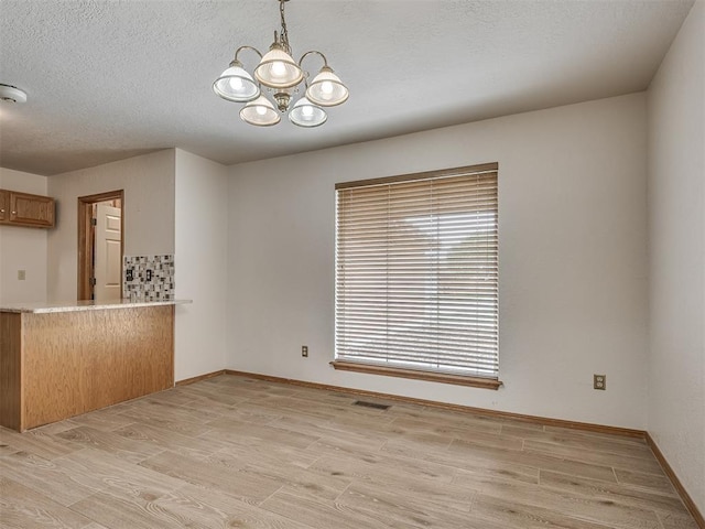 unfurnished dining area with an inviting chandelier, baseboards, a textured ceiling, and light wood-style flooring