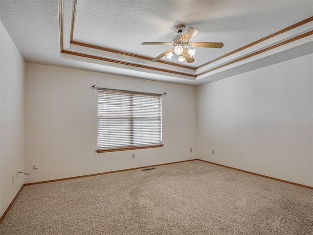 empty room featuring a ceiling fan, a textured ceiling, a tray ceiling, and carpet