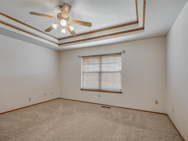 carpeted empty room featuring ceiling fan, a textured ceiling, baseboards, a tray ceiling, and visible vents
