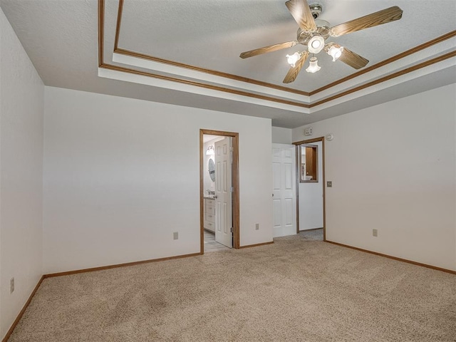 carpeted empty room with baseboards, a ceiling fan, a raised ceiling, and crown molding