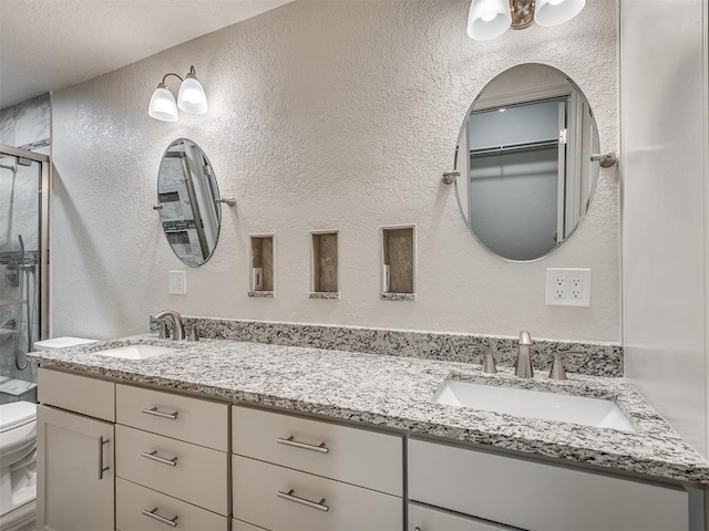 bathroom featuring a sink, a textured wall, toilet, and a shower stall