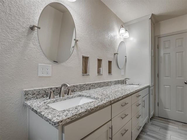 full bath with double vanity, a textured wall, a sink, and a textured ceiling