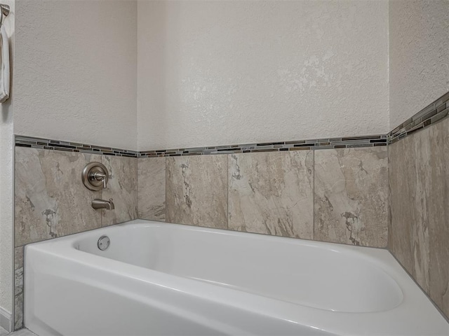 bathroom featuring a textured wall and a garden tub