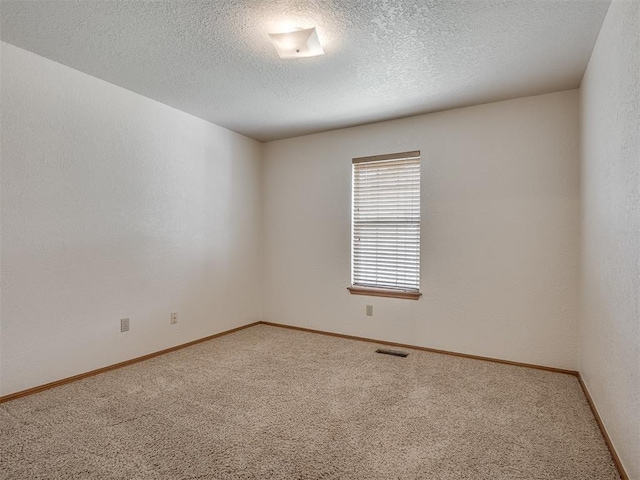 carpeted spare room with baseboards, a textured ceiling, and visible vents
