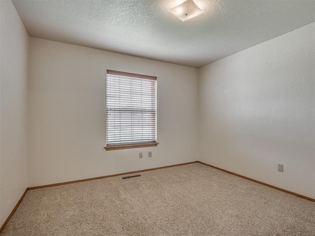 carpeted empty room featuring a textured ceiling, baseboards, and visible vents