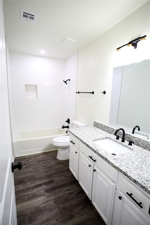 bathroom featuring visible vents, vanity, wood finished floors, toilet, and shower / bath combination