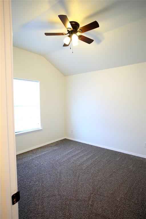 spare room with dark carpet, baseboards, ceiling fan, and vaulted ceiling