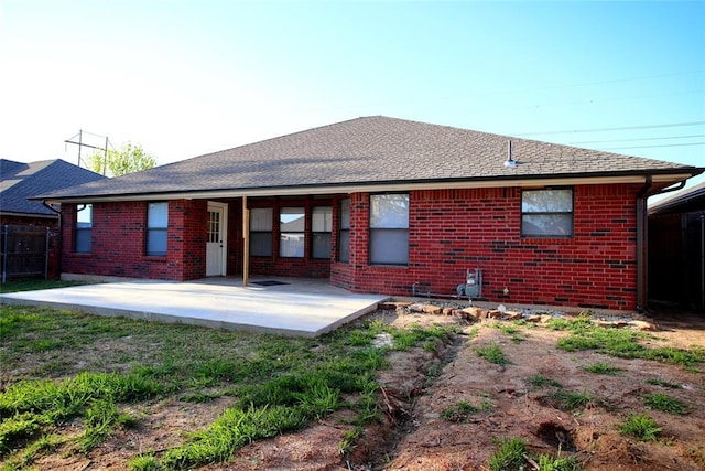 rear view of house featuring fence, a patio, a shingled roof, and brick siding