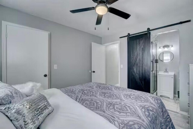 bedroom with a ceiling fan, a barn door, a sink, and ensuite bath