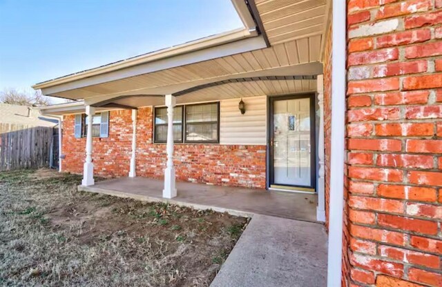 doorway to property featuring brick siding and fence