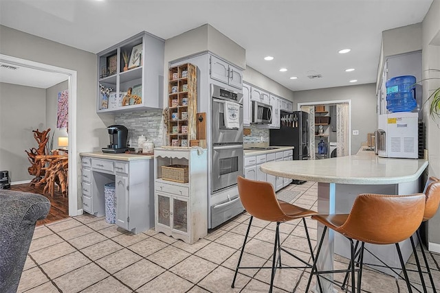 kitchen with light countertops, backsplash, a warming drawer, and stainless steel appliances