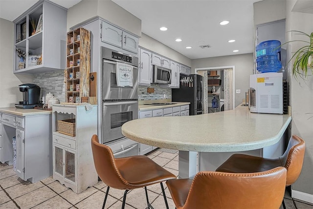 kitchen with decorative backsplash, black appliances, a peninsula, and a kitchen bar