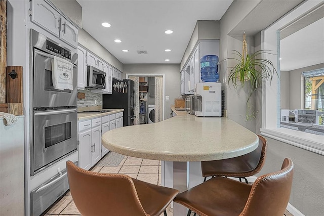 kitchen featuring appliances with stainless steel finishes, light countertops, a peninsula, recessed lighting, and a warming drawer