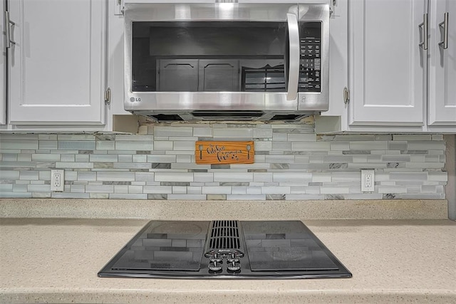 kitchen featuring decorative backsplash, black electric cooktop, stainless steel microwave, and white cabinetry