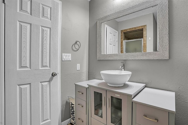 full bath featuring vanity, a shower with door, and a textured wall