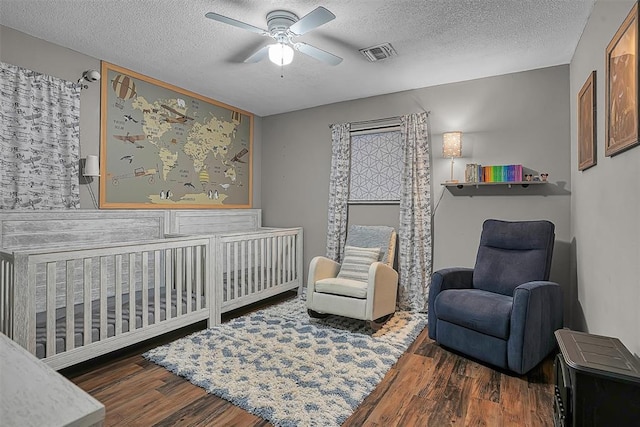 bedroom featuring visible vents, wood finished floors, ceiling fan, a textured ceiling, and a nursery area