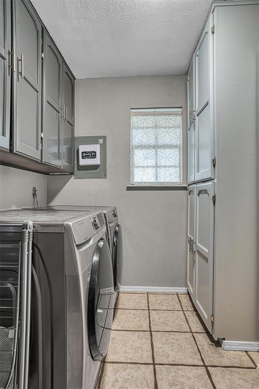 laundry room with baseboards, washer and clothes dryer, a textured ceiling, cabinet space, and light tile patterned floors