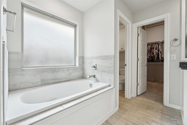 full bath featuring a walk in closet, a garden tub, and toilet