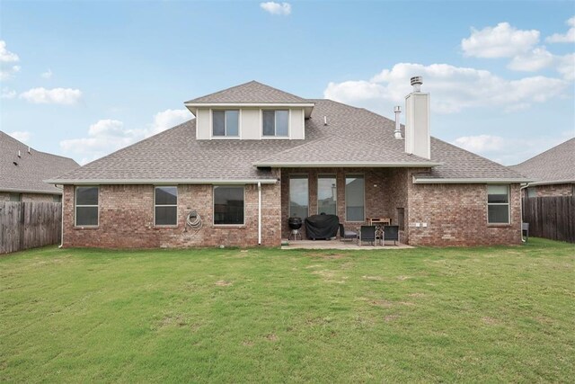 rear view of house with a chimney, roof with shingles, a fenced backyard, a yard, and a patio