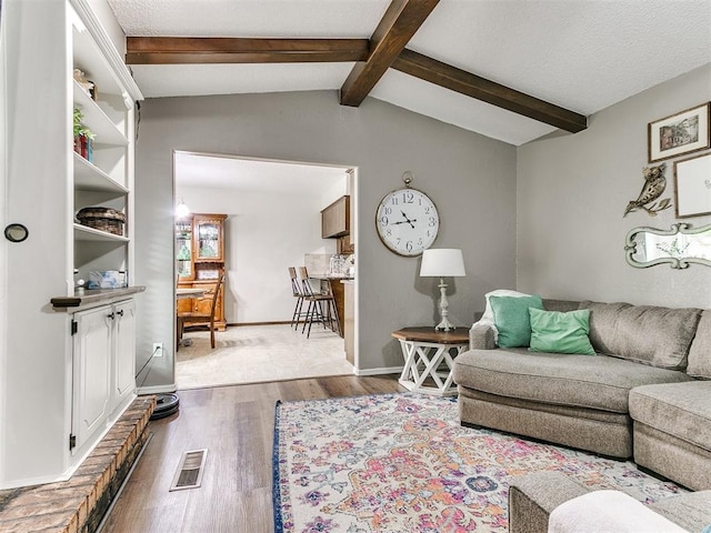 living room featuring visible vents, lofted ceiling with beams, baseboards, and wood finished floors