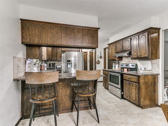 kitchen with decorative backsplash, dark brown cabinetry, a peninsula, under cabinet range hood, and stainless steel appliances